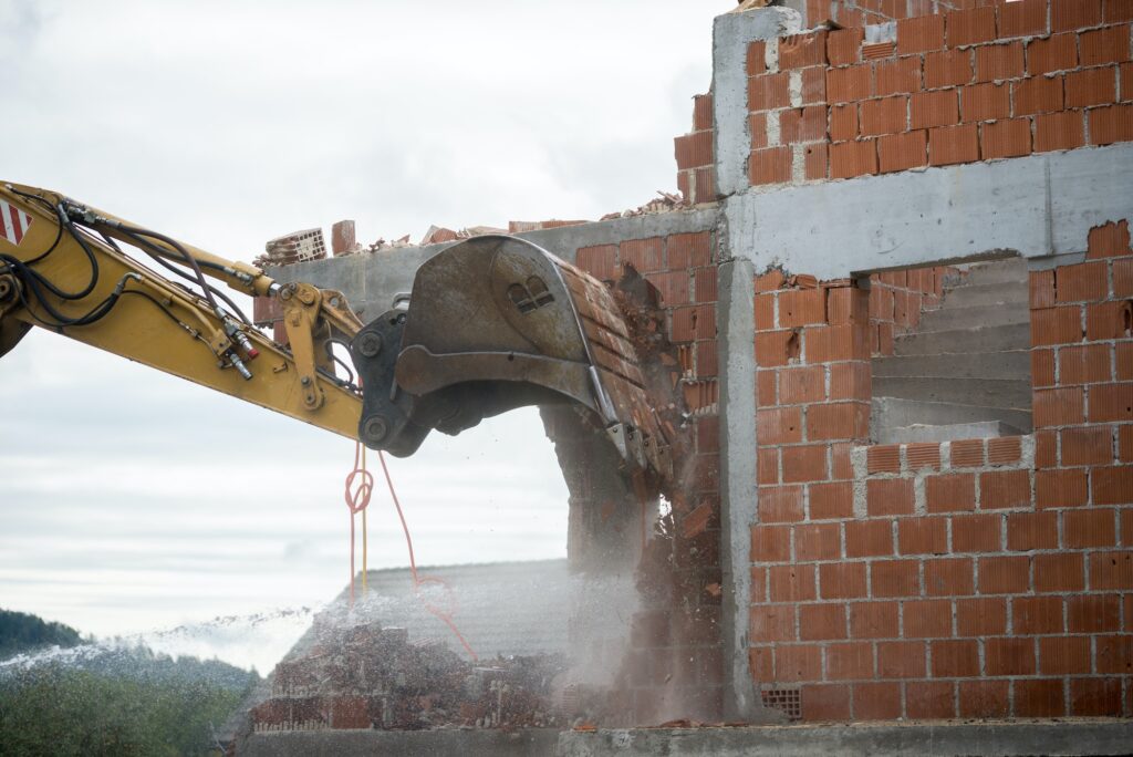 Backhoe demolishing a brick house